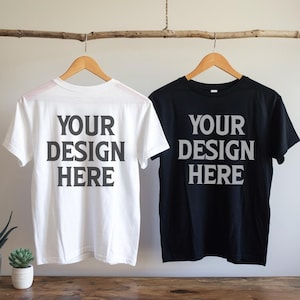 Könnte beinhalten: Zwei leere T-Shirts hängen an einem Holzast. Die T-Shirts sind weiß und schwarz. Der Text "YOUR DESIGN HERE" ist auf beiden Shirts gedruckt.