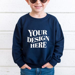 Puede incluir: Una sudadera azul marino con el texto blanco "YOUR DESIGN HERE". La sudadera es de cuello redondo y la lleva una persona con gafas de sol y vaqueros azules.