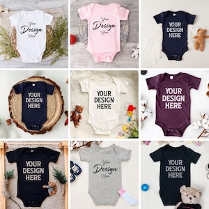 Puede incluir: Nueve bodies de bebé en diferentes colores, incluyendo blanco, rosa, negro, gris y granate. Cada body tiene mangas cortas y cierre a presión. Los bodies presentan el texto "Your Design Here" impreso en negro.
