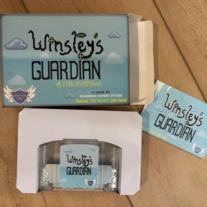 May include: A video game box set for "Winsley's Guardian" with a light blue background, pixelated clouds, and the game title in a whimsical font. The set includes the game cartridge and a small card.