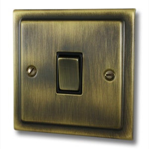 May include: A brushed antique brass light switch with a black toggle switch. The switch has a rectangular shape and is surrounded by a decorative frame.