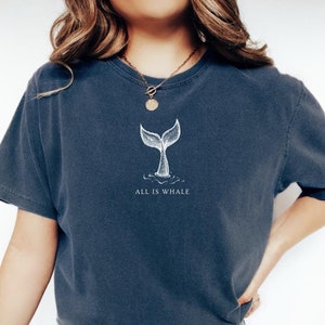 May include: A navy blue t-shirt with a white whale tail graphic and the text "All is Whale".