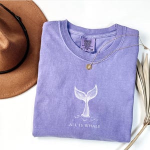 May include: A lavender t-shirt with a white whale tail graphic and the text "All is Whale".