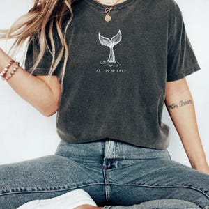 May include: A dark gray t-shirt with a white whale tail graphic and the text "All is Whale".