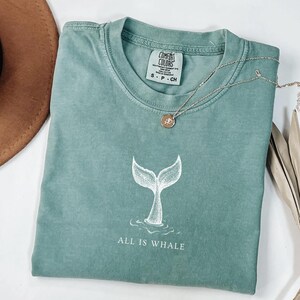 May include: A teal blue t-shirt with a white whale tail graphic and the text "All is Whale".