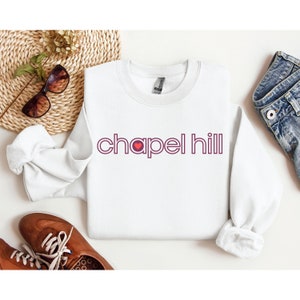 May include: White sweatshirt with a maroon graphic that says "chapel hill" with a red heart in the "a".