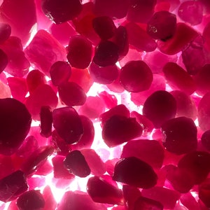 Puede incluir: Una vista de cerca de un mont&oacute;n de piedras preciosas rosas sueltas. Las piedras preciosas son de varias formas y tama&ntilde;os, y est&aacute;n iluminadas desde abajo, creando una superficie brillante y reflectante.