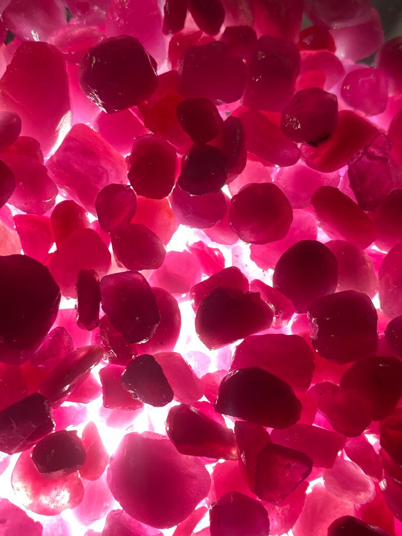 Puede incluir: Una vista de cerca de un mont&oacute;n de piedras preciosas rosas sueltas. Las piedras preciosas son de varias formas y tama&ntilde;os, y est&aacute;n iluminadas desde abajo, creando una superficie brillante y reflectante.