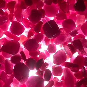 Puede incluir: Una vista cercana de una colecci&oacute;n de piedras preciosas rosadas y rojas. Las piedras preciosas son de varias formas y tama&ntilde;os, y est&aacute;n esparcidas sobre una superficie blanca.