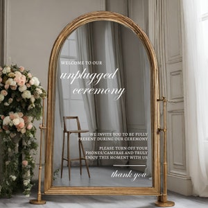 May include: A gold-framed arched mirror with a sign that reads "Welcome to our unplugged ceremony. We invite you to be fully present during our ceremony. Please turn off your phones/cameras and truly enjoy this moment with us. Thank you."