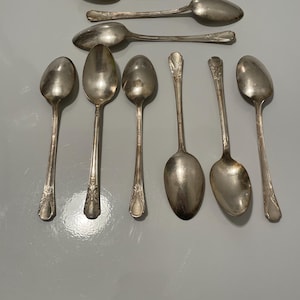 Può includere: Un set di dieci cucchiai d'argento con manici decorati. I cucchiai sono disposti in due file, con cinque cucchiai in ogni fila. I cucchiai sono tutti della stessa dimensione e forma.