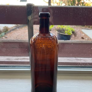 May include: A brown glass bottle with the text "Witter Springs Water" embossed on the front. The bottle is sitting on a white windowsill.