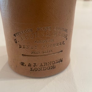 May include: A brown stoneware bottle with the text "VITREOUS STONE BOTTLES, J. BOURNE & SON, PATENTEES, DENBY POTTERY, NEAR DERBY. & J. ARNO LONDON" embossed on the side.