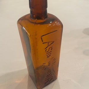 May include: A brown glass bottle with a square shape and a label that reads "KING'S" and "LAXATIVE" with a line under the word "LAXATIVE".