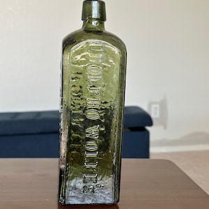 May include: A vintage green glass bottle with a textured surface. The bottle has the text "J.W. WOLFE'S" embossed on the front.