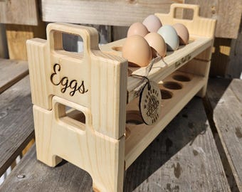 Pode incluir: Um suporte de ovos de madeira com duas camadas, cada uma com seis ranhuras. A camada superior tem cinco ovos, e a camada inferior está vazia. O suporte é etiquetado como "Eggs" e "Farm Fresh Eggs".