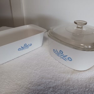 May include: A white casserole dish with a blue floral design and a matching glass lid. The dish is on a white towel.