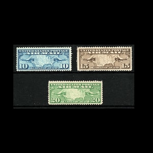 May include: Three vintage United States postage stamps. The stamps are rectangular with the text "UNITED STATES POSTAGE AIRMAIL" at the top. The stamps are blue, brown, and green, with values of 10, 15, and 20 cents.