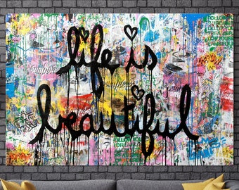 May include: A colorful abstract painting with the words "Life is beautiful" in black paint. The painting is on a canvas and is hanging on a brick wall. There is a gray couch and a yellow throw blanket in the foreground.