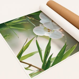 May include: A print depicting white orchid flowers and green bamboo leaves. The print is partially rolled, with two cylindrical tubes in white and brown cardboard. The image has a soft, natural aesthetic.