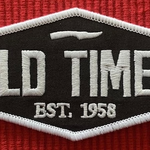 May include: A black and white embroidered patch with the text "OLD TIMER EST. 1958" in a white outline.