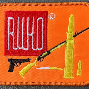 May include: Orange patch with a red square containing the white text "RUKO". The patch features yellow and black illustrations of a rifle, bullets, and a handgun. The patch has a stitched border.