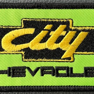 May include: Embroidered patch with a neon green background and black border. The patch features the word "City" in yellow script above the Chevrolet logo, with "CHEVROLET" embroidered in black below. The patch is rectangular.