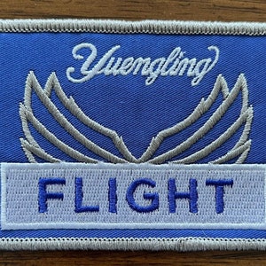 May include: A blue and white embroidered patch with the text "Yuengling Flight" and a silver embroidered wing design.