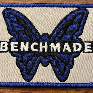 May include: A white patch with a blue border featuring a blue and black butterfly with the word "BENCHMADE" in white letters.