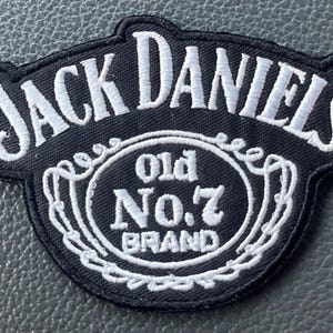 May include: Black and white embroidered patch featuring the text "JACK DANIEL'S" arched across the top. Below, an oval design reads "Old No. 7 BRAND" in white lettering. The patch has a black background and a decorative white border.