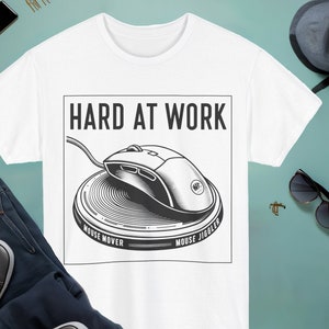 May include: White t-shirt with a black and white illustration of a computer mouse on a circular mouse pad. The text "HARD AT WORK" is above the illustration. The text "MOUSE MOVER" is below the left side of the mouse pad and "MOUSE JIGGLER" is below the right side of the mouse pad.