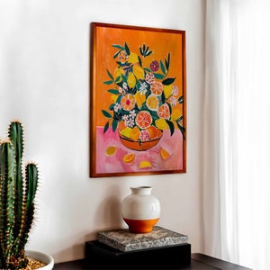May include: A framed painting of a still life featuring a bowl of lemons and flowers on a pink background. The bowl is brown and the lemons are yellow with green leaves. The flowers are pink, white, and yellow.
