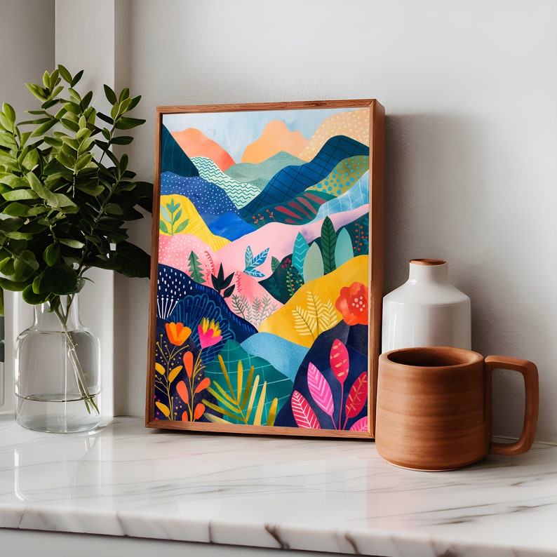 May include: A framed art print depicting a colourful landscape with rolling hills and vibrant flora. The artwork features blues, pinks, yellows, and oranges, with a wooden frame. The print is displayed on a white marble surface.