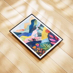 May include: A rectangular framed art print with an abstract landscape design. The artwork features a vibrant mix of colours, including blue, pink, and yellow. The black frame contrasts with the colourful print, displayed on a wooden surface.