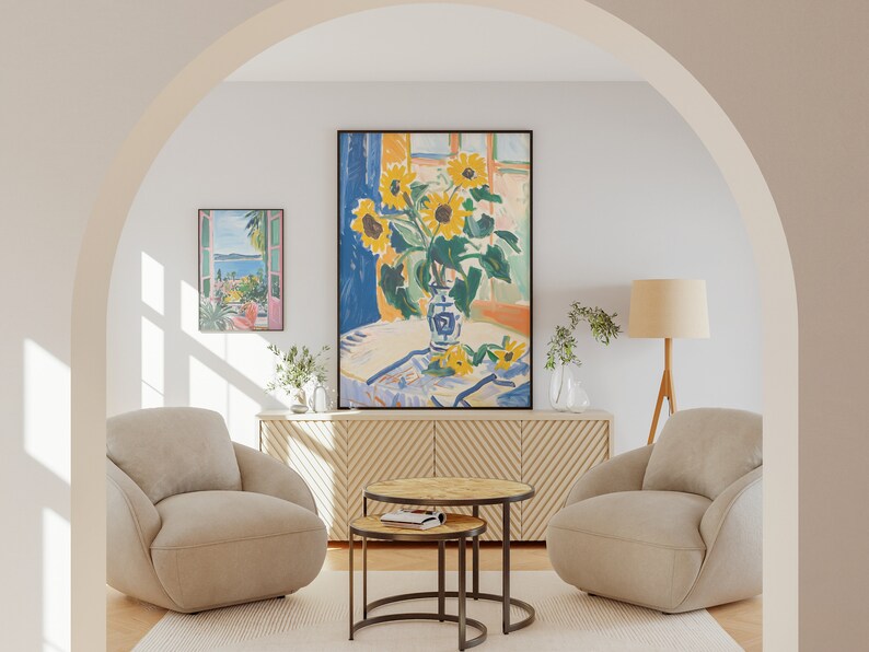 May include: Two beige armchairs with a wooden floor and a rug. A wooden table with a glass top sits between the chairs. A large painting of sunflowers in a vase sits above a wooden cabinet with a chevron pattern. A smaller painting of a landscape with a window frame is on the wall to the left of the large painting. A floor lamp with a beige shade and a wooden tripod base is to the right of the chairs.