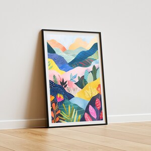 May include: A framed art print with a vibrant landscape illustration. The artwork shows rolling hills and mountains in shades of blue, pink, yellow, and orange, with detailed floral and foliage elements. The print is set in a black frame.