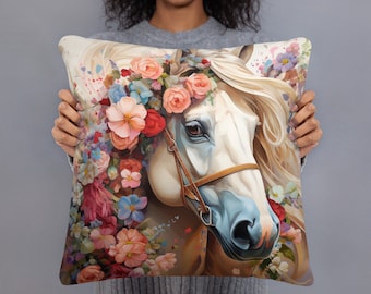 Può includere: Cuscino quadrato con un'illustrazione ad acquerello di un cavallo bianco adornato da una corona floreale. Il cavallo ha un muso blu e una briglia marrone. Il cuscino è decorato con fiori rosa, rossi e blu.