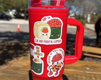 May include: Red reusable tumbler with a lid and handle. The tumbler has several stickers on it, including one that says "The Roe Mantic Combo" and another that says "You Soy Complete Me".