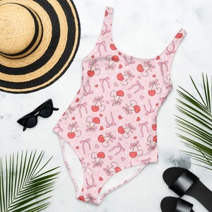 Può includere: Costume da bagno intero rosa con stampa a ciliegie e fiocchi. Il costume da bagno ha una scollatura rotonda e spalline sottili.