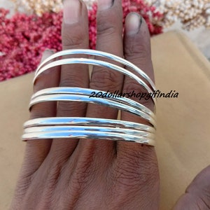May include: Set of six silver bangles stacked on a hand. The bangles are smooth and shiny.