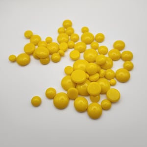 May include: A large pile of yellow wax beads, used for waxing, are scattered on a white surface.
