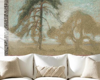 May include: A woven throw blanket featuring a landscape scene with trees in shades of green, brown, and beige. The artwork has a soft, painterly quality. The blanket has a fringed edge and is displayed on a white sofa with beige pillows.