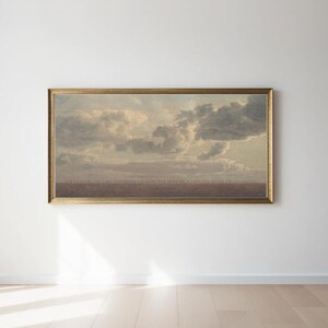 May include: A framed landscape painting featuring a cloudy sky with a golden frame. The artwork depicts a dramatic sky with dark and light gray clouds. The bottom of the painting has a brown area. The text at the bottom is blurry.
