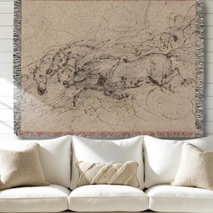 May include: A woven throw blanket featuring a sketch of running horses in shades of brown and black. The artwork has a vintage aesthetic, with visible lines and shading. The blanket has a fringed edge and is displayed on a white couch.