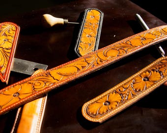 May include: Four leather straps with intricate floral designs. The straps are brown and have a black trim. The straps are arranged on a dark surface.