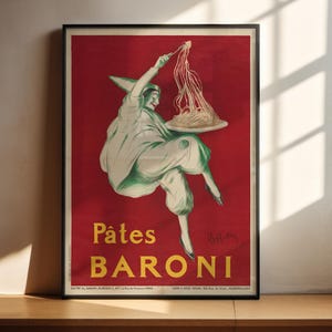 Puede incluir: Un póster enmarcado de estilo vintage con fondo rojo y una ilustración central de una figura con traje blanco y verde levantando un tenedor de espaguetis de un plato. El texto Pâtes BARONI aparece en grandes letras amarillas en la parte inferior.