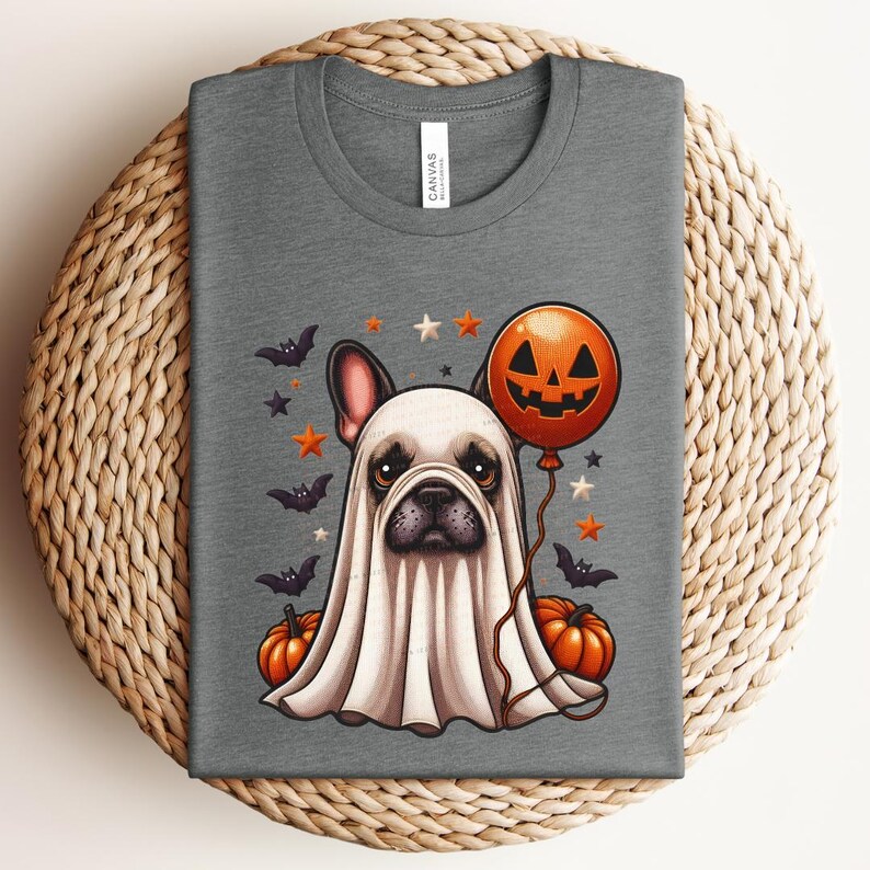 Pu&ograve; includere: Una maglietta grigia con una simpatica illustrazione di un bulldog francese vestito da fantasma per Halloween. Il bulldog indossa un costume da fantasma bianco con un palloncino a forma di zucca e pipistrelli e stelle sullo sfondo.