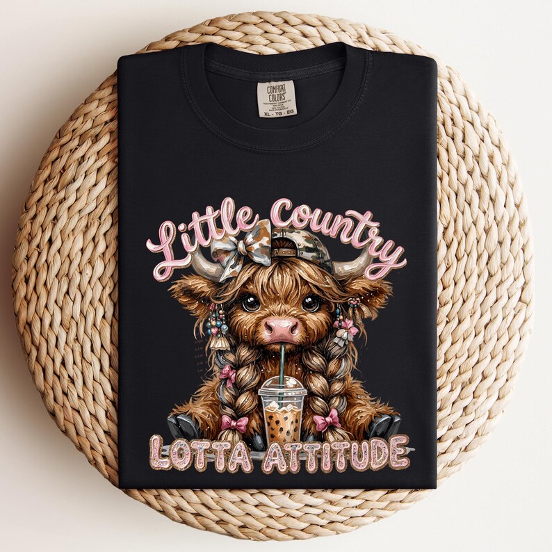 May include: Black t-shirt featuring a cartoon Highland cow with braids, a bow, and a hat, drinking from a beverage cup. The text "Little Country Lotta Attitude" is displayed in pink script.