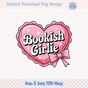 Op de afbeelding: Een roze hartvormig kussen met een witte rand en een gekrulde zoom. Het kussen heeft de tekst "Bookish Girlie" in een retro-lettertype. Een roze strik is aan de onderkant van het kussen bevestigd.