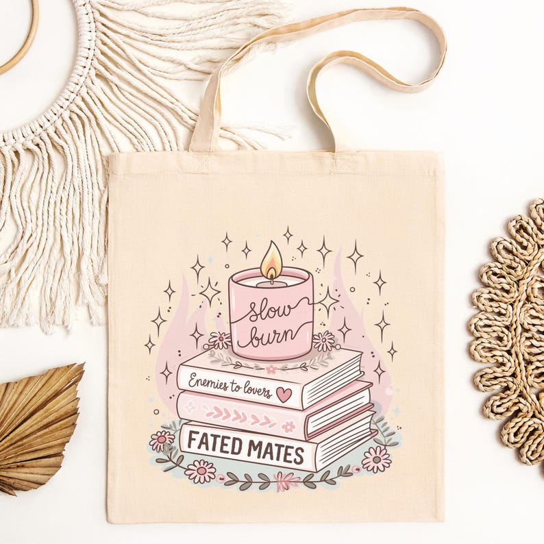 May include: Cream canvas tote bag with a pink candle design, the words "slow burn", and a flame. Below the candle are three books with the titles "Enemies to lovers" and "Fated mates". The design includes floral and star accents.